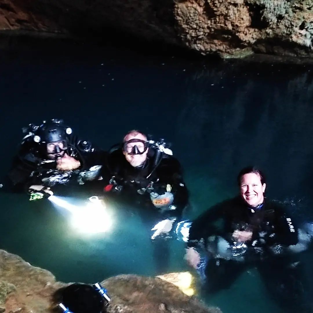 Team surfacing in cave with torch beams